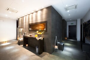 A modern reception area with a dark reception desk, a glass display case, and a small seating area with a chair and a white cube.