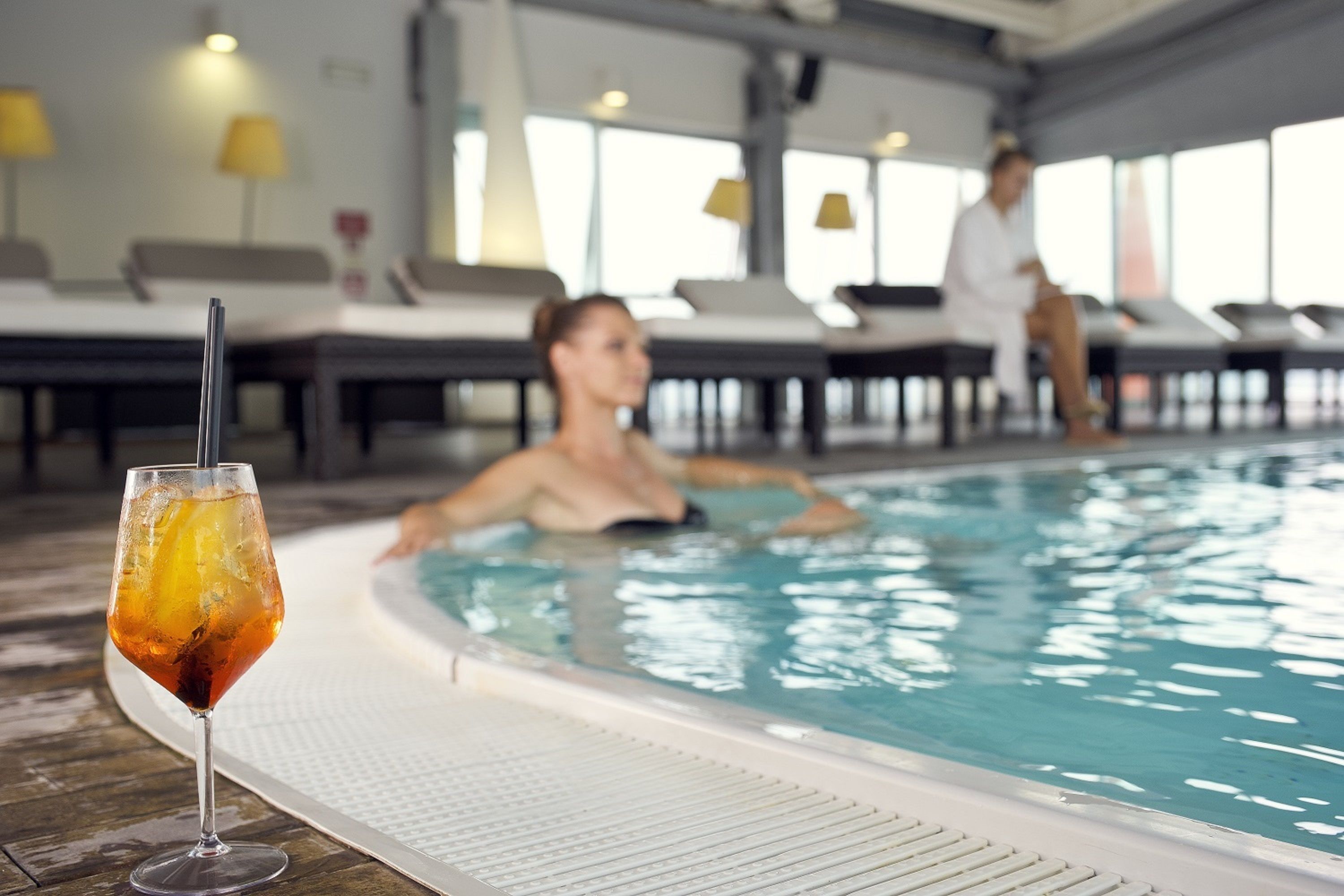 Una piscina con sillas de descanso y un vaso de bebida helada en la terraza.
