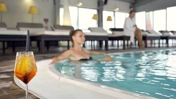 Una piscina con lettini e un bicchiere di bevanda fresca sul bordo.