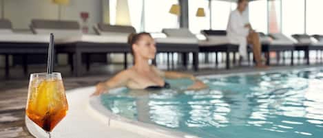 A swimming pool with lounge chairs and a glass of iced drink on the deck.
