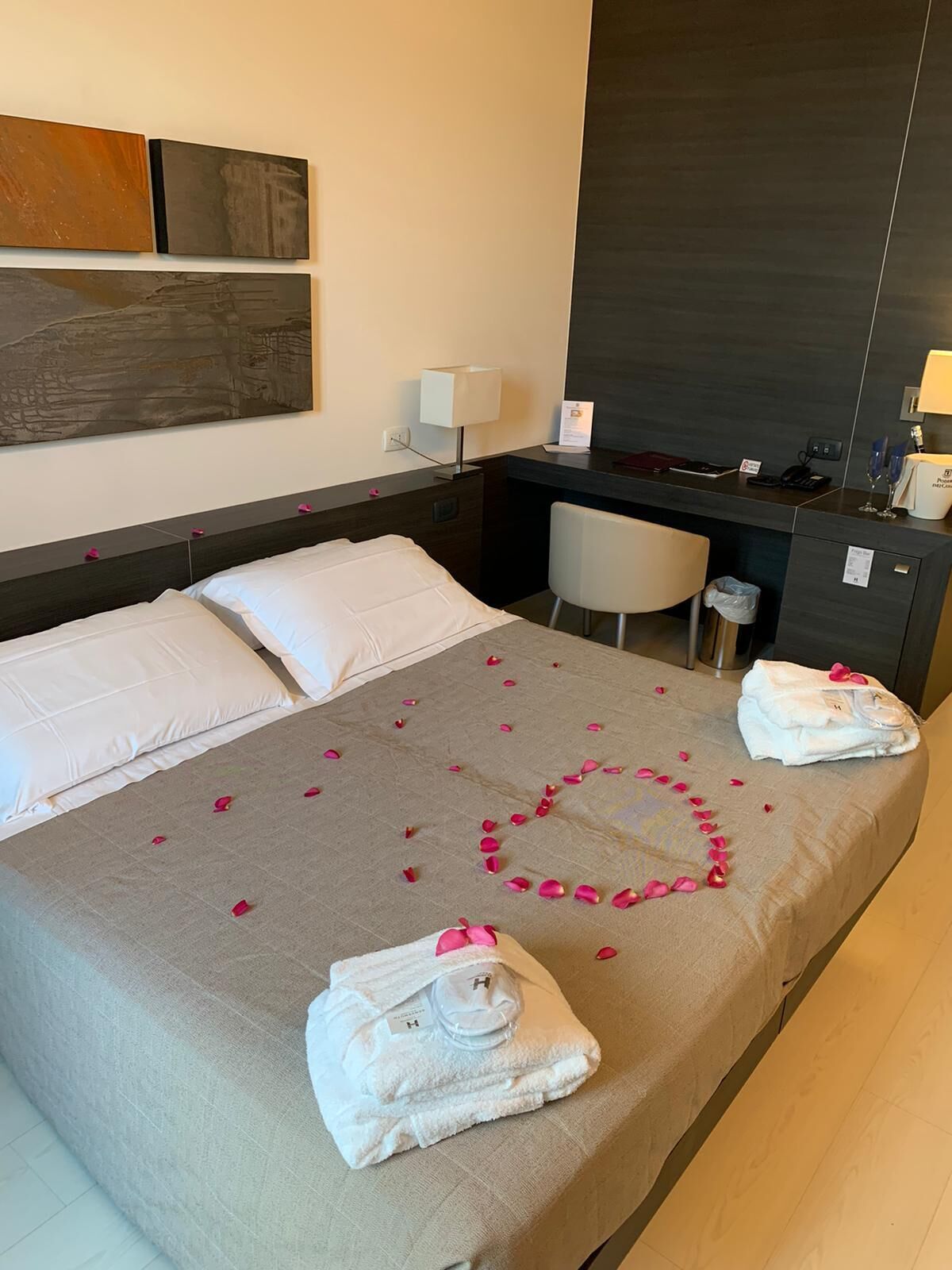Une chambre d’hôtel avec un lit, un bureau et une chaise. Il y a des serviettes et une bouteille sur le lit.