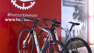 Un mur rouge avec une enseigne indiquant « Bikeroom », deux vélos et une affiche faisant la promotion d’un événement cycliste.