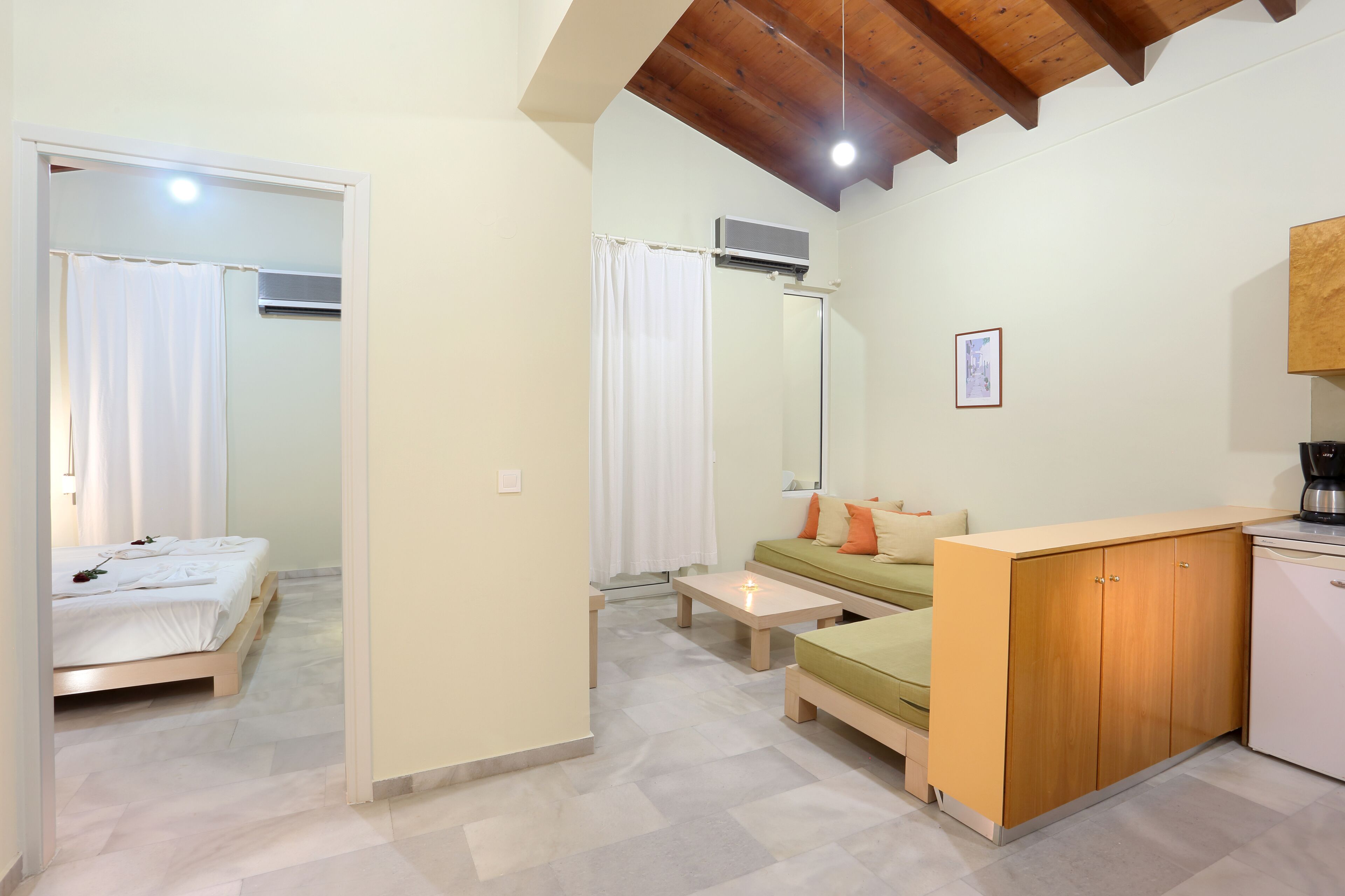 Quarto moderno e bem iluminado com cama, sofá, pequena mesa e um espaço de cozinha compacta.