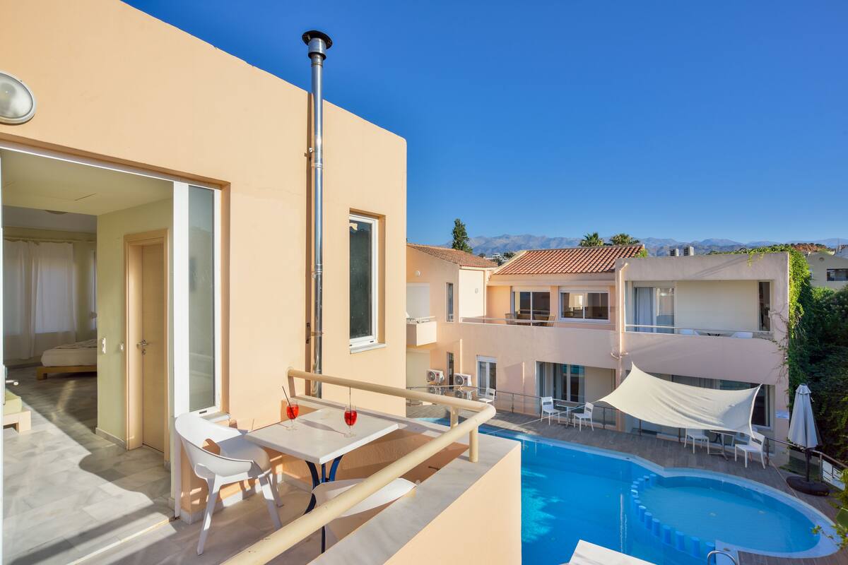 A modern hotel with a rooftop pool, outdoor seating, and a view of mountains.