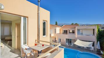 A modern hotel with a rooftop pool, outdoor seating, and a view of mountains.