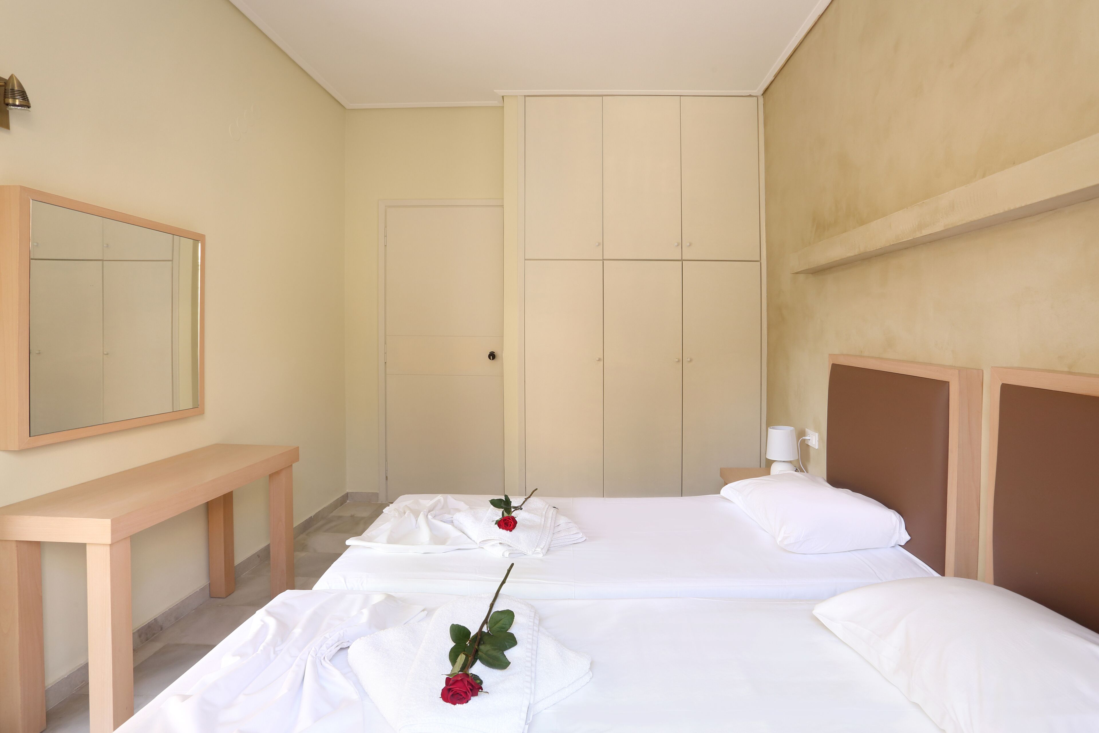 A hotel room with two beds, a wooden bench, a mirror, and a door.