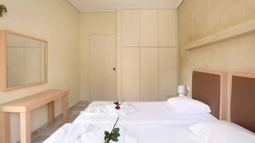 A hotel room with two beds, a wooden bench, a mirror, and a door.
