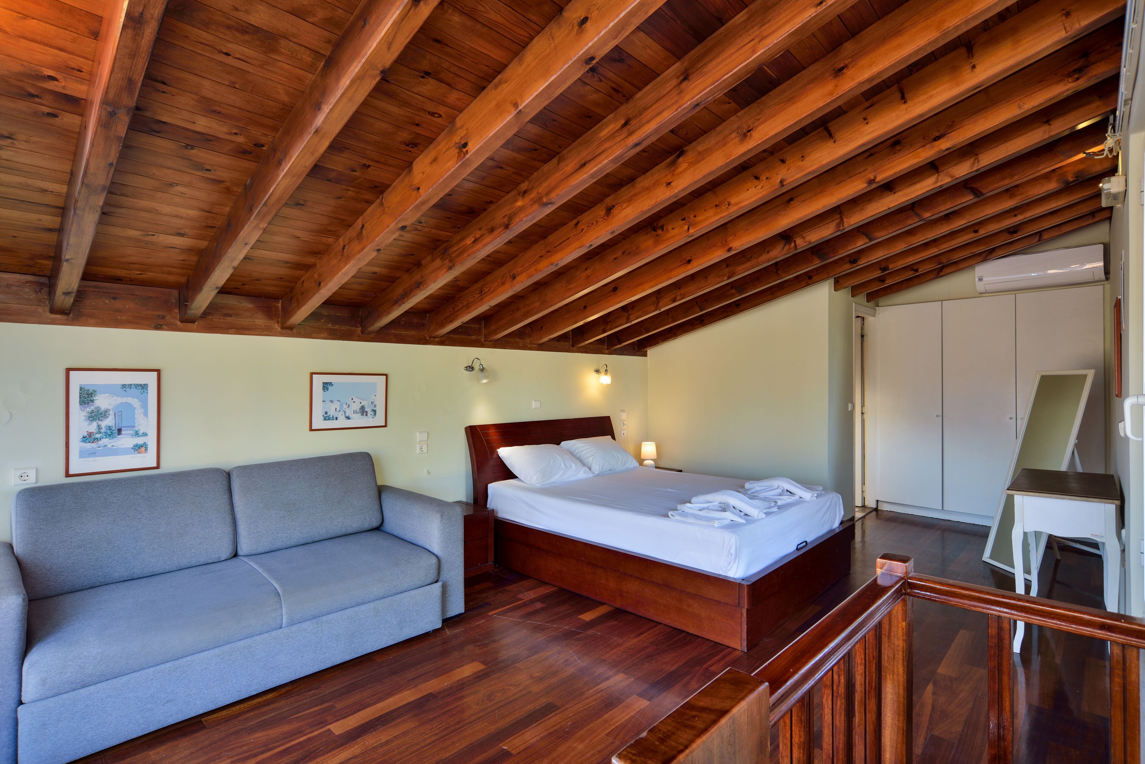 A bedroom with a wooden ceiling, a bed, a gray sofa, and a small table.