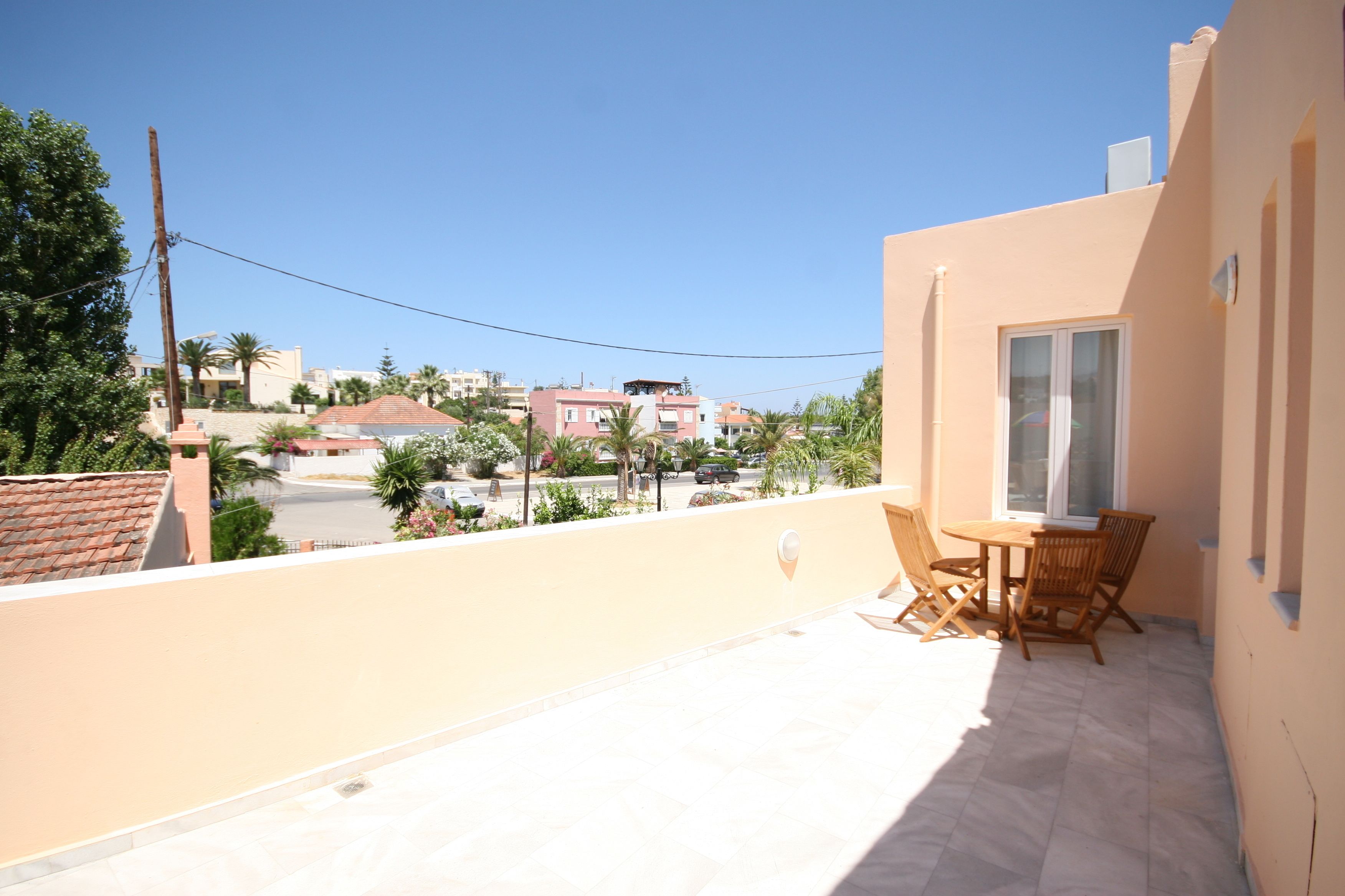 A balcony with a table and chairs, overlooking a residential area with houses and palm trees.