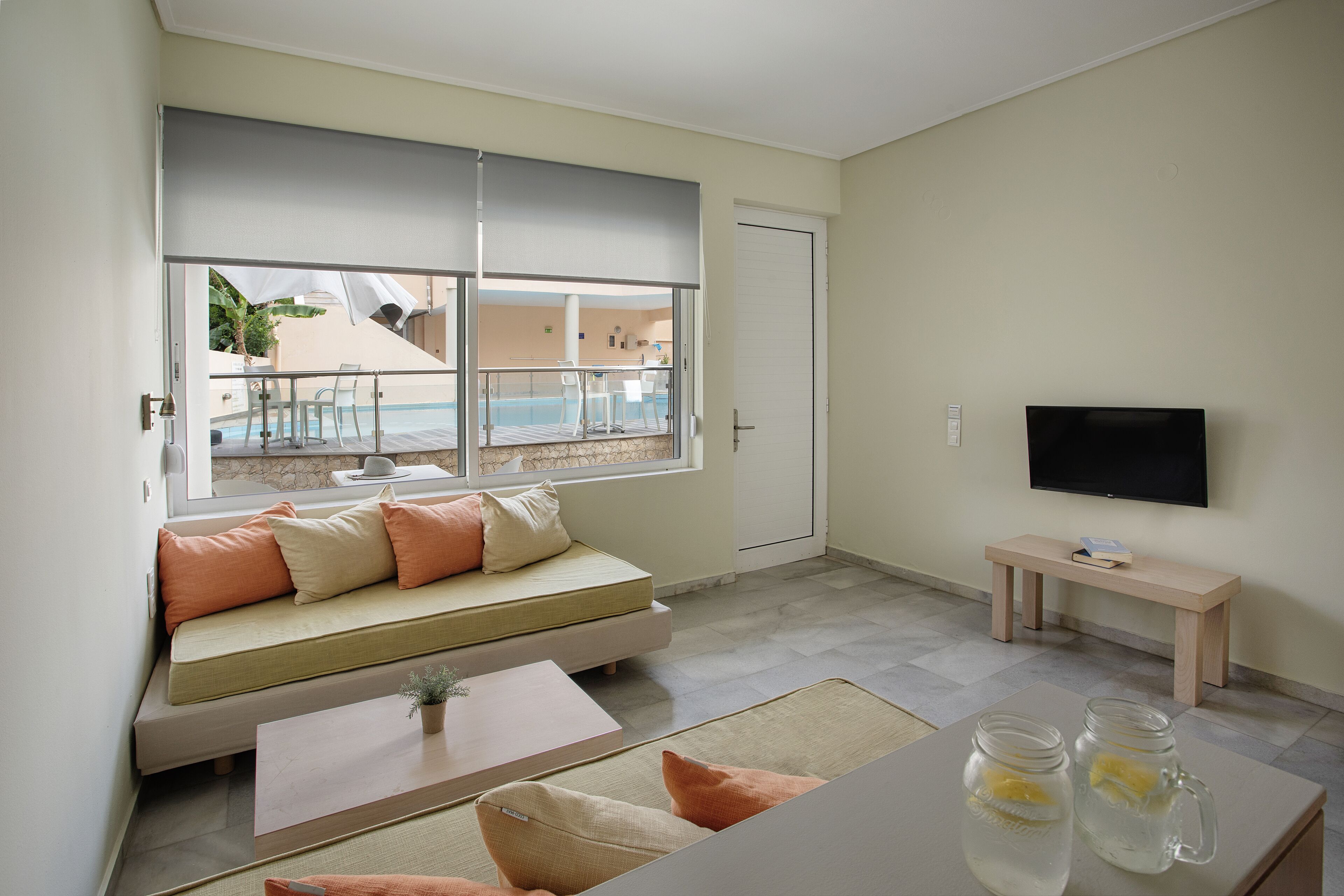 A modern living room with a sofa, a coffee table, a TV, and a view of an outdoor pool area.