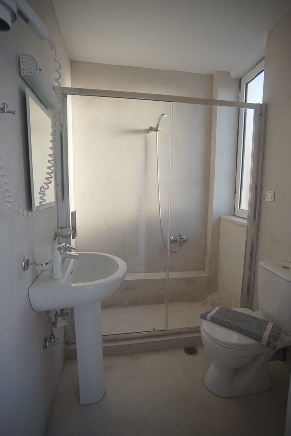Un baño con lavamanos blanco, inodoro y ducha con mampara de vidrio.
