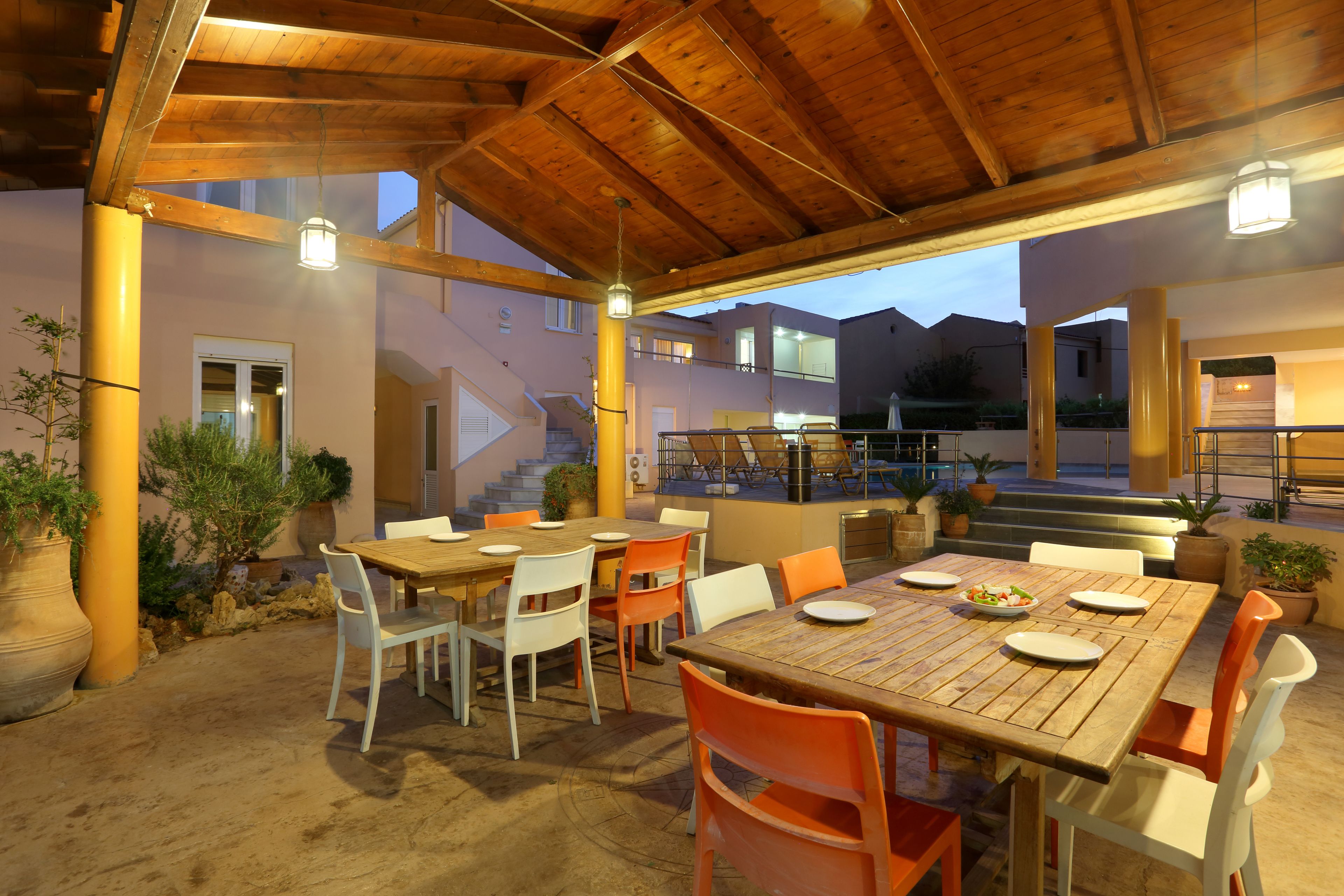 An outdoor dining area with wooden tables and chairs, potted plants, and a staircase leading to an upper level.