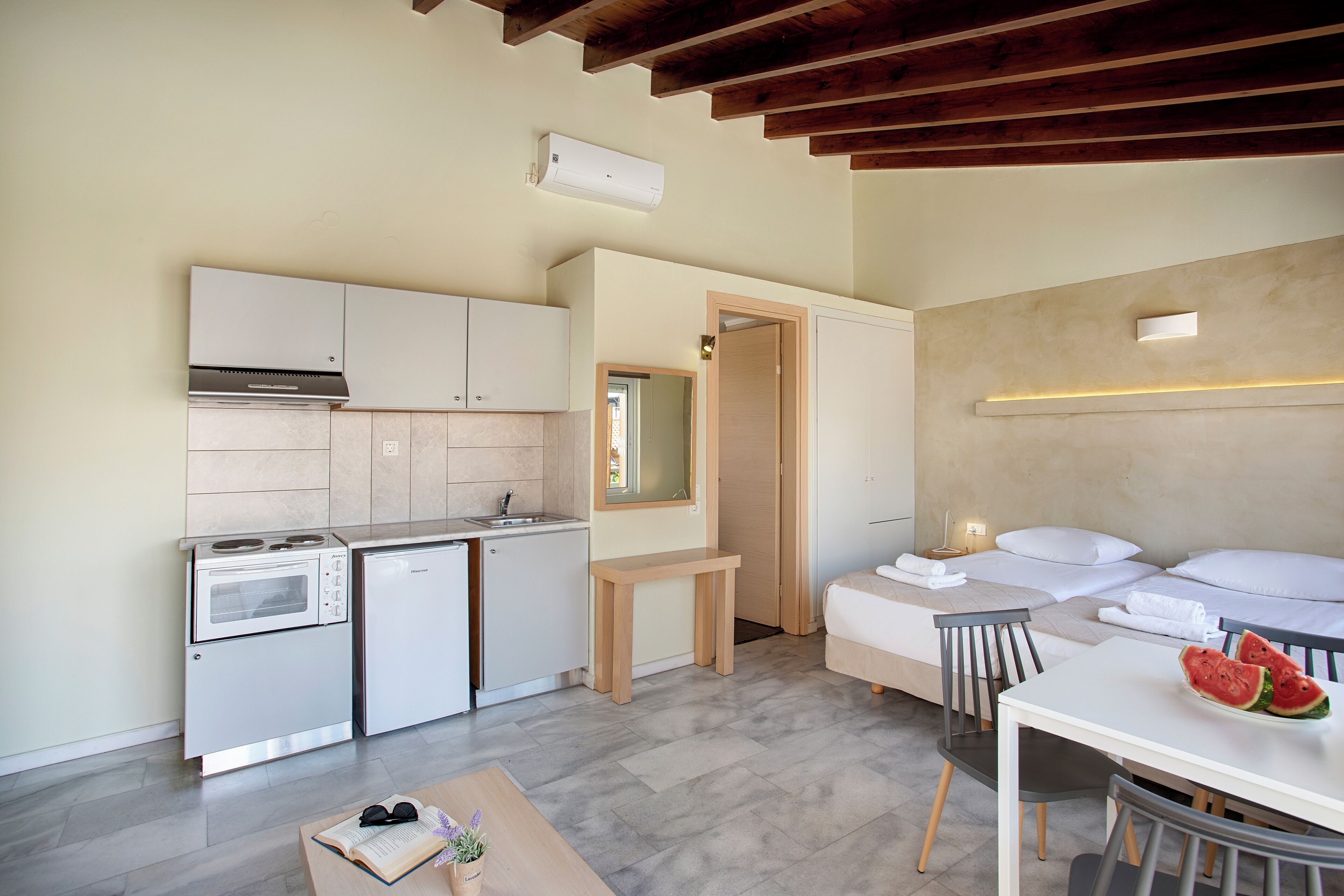 Une cuisine compacte équipée d’un four à micro-ondes, d’un four et d’un évier, un petit coin repas avec une table et des chaises, et une chambre avec un lit et une table de chevet.