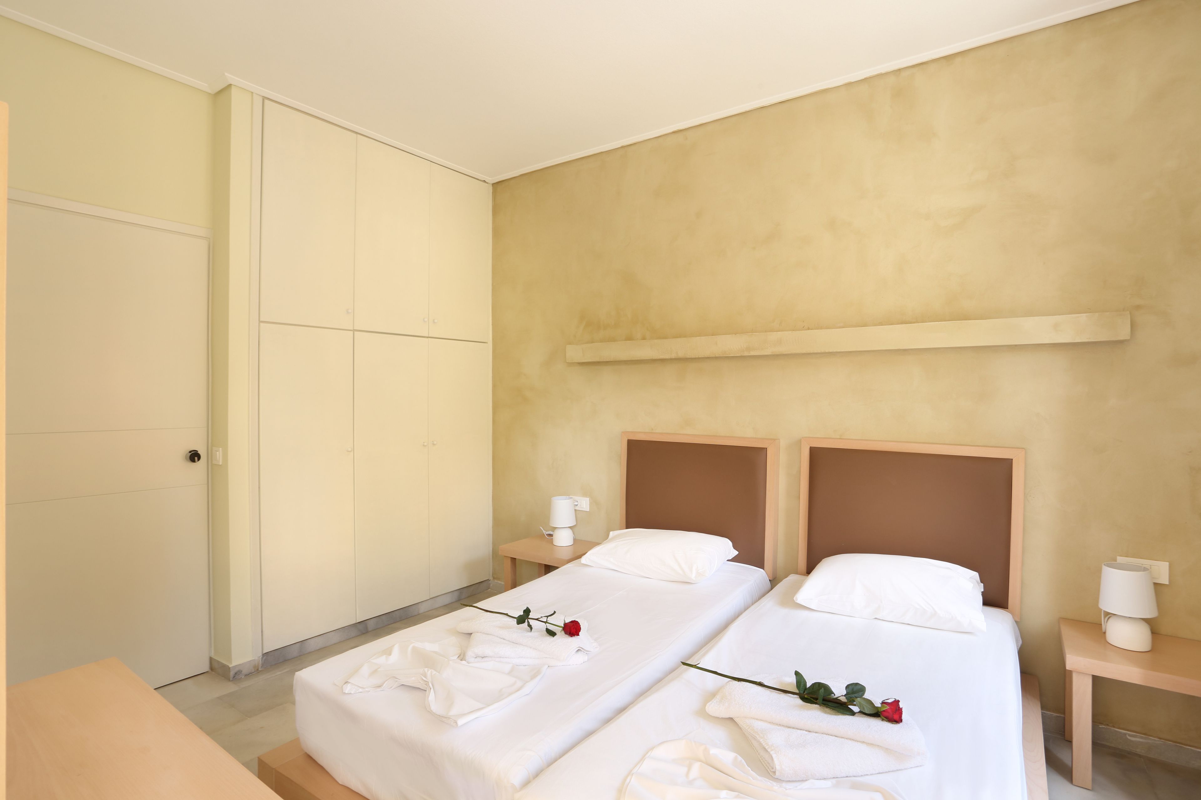 A hotel room with two beds, a bedside table with a lamp, and a wardrobe.