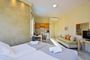 Ein Hotelzimmer mit zwei Betten, einer Küchenzeile, einem Fernseher und einem Sofa.