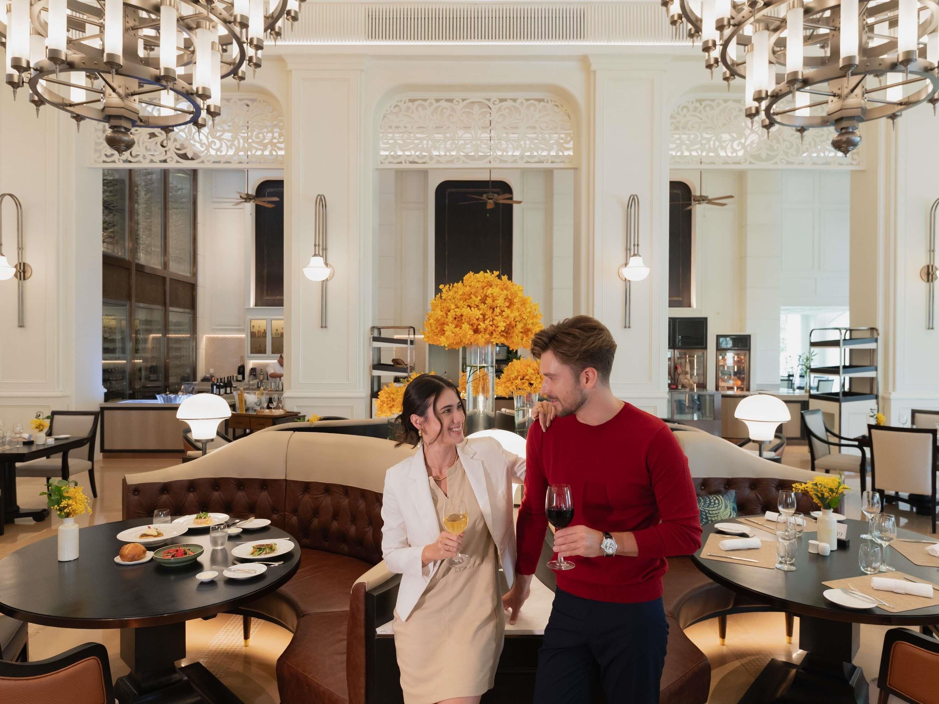 A luxurious dining area with high ceilings, ornate chandeliers, and a central floral arrangement.