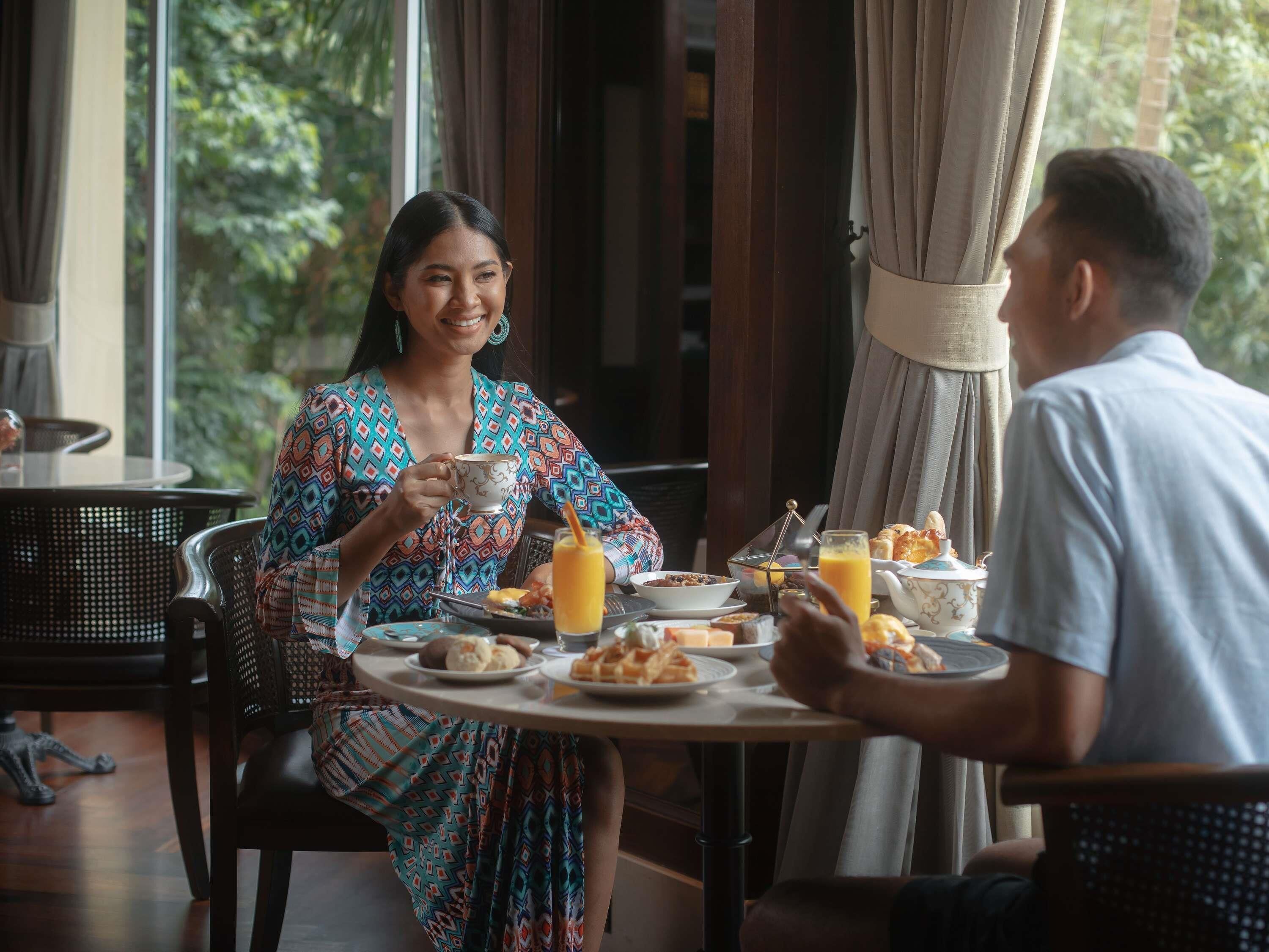 Comedor con una mesa redonda dispuesta para dos personas, con alimentos para el desayuno como cruasanes, un bol de frutas y un vaso de jugo de naranja.