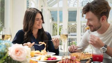 A couple dining at a table with a variety of dishes and drinks, in a bright, open space with large windows.