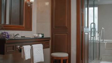 Une salle de bain avec un meuble-lavabo en bois, un miroir, un porte-serviettes, une cabine de douche en verre et un tabouret.