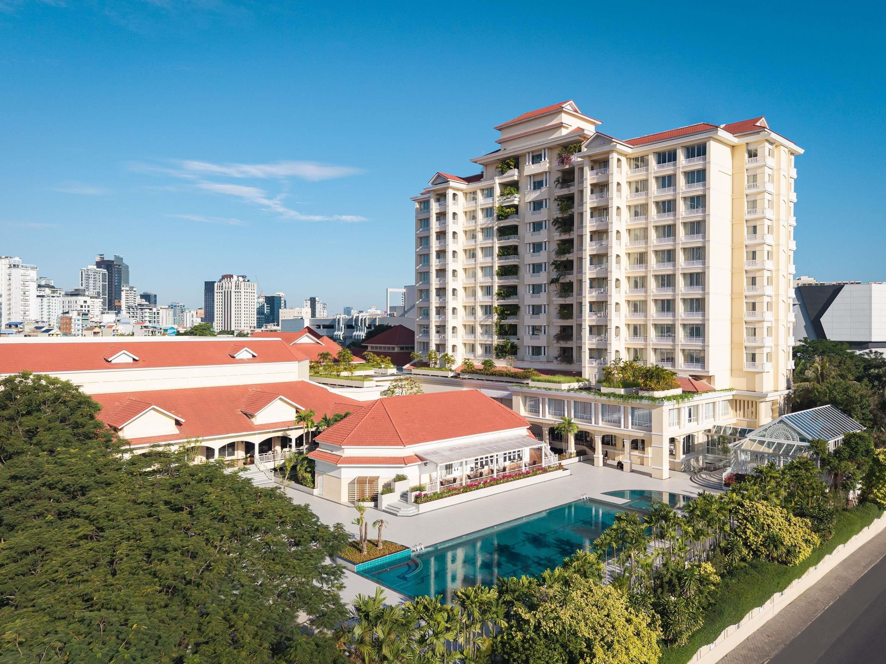 Un hotel moderno de gran altura con varios balcones, una piscina y el horizonte urbano al fondo.