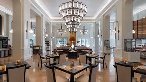 A spacious dining area with multiple tables and chairs, a large chandelier, and a view of the kitchen in the background. - Sofitel Phnom Penh Phokeethra (Phnom Penh)