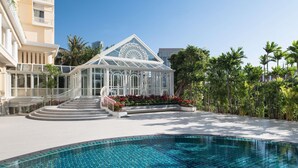 A resort with a swimming pool, a glass conservatory, and a palm tree-lined walkway. - Sofitel Phnom Penh Phokeethra (Phnom Penh)