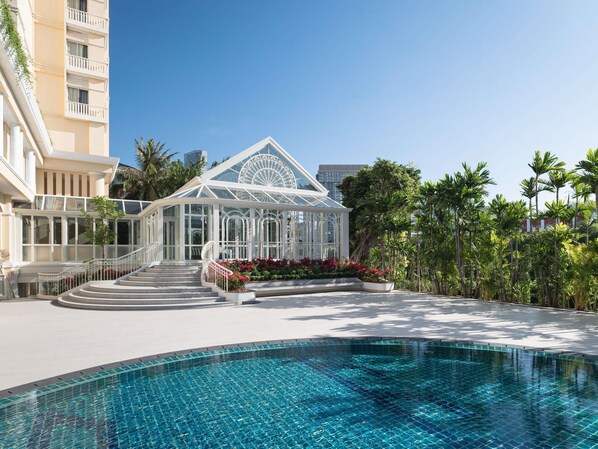 A resort with a swimming pool, a glass conservatory, and a palm tree-lined walkway.