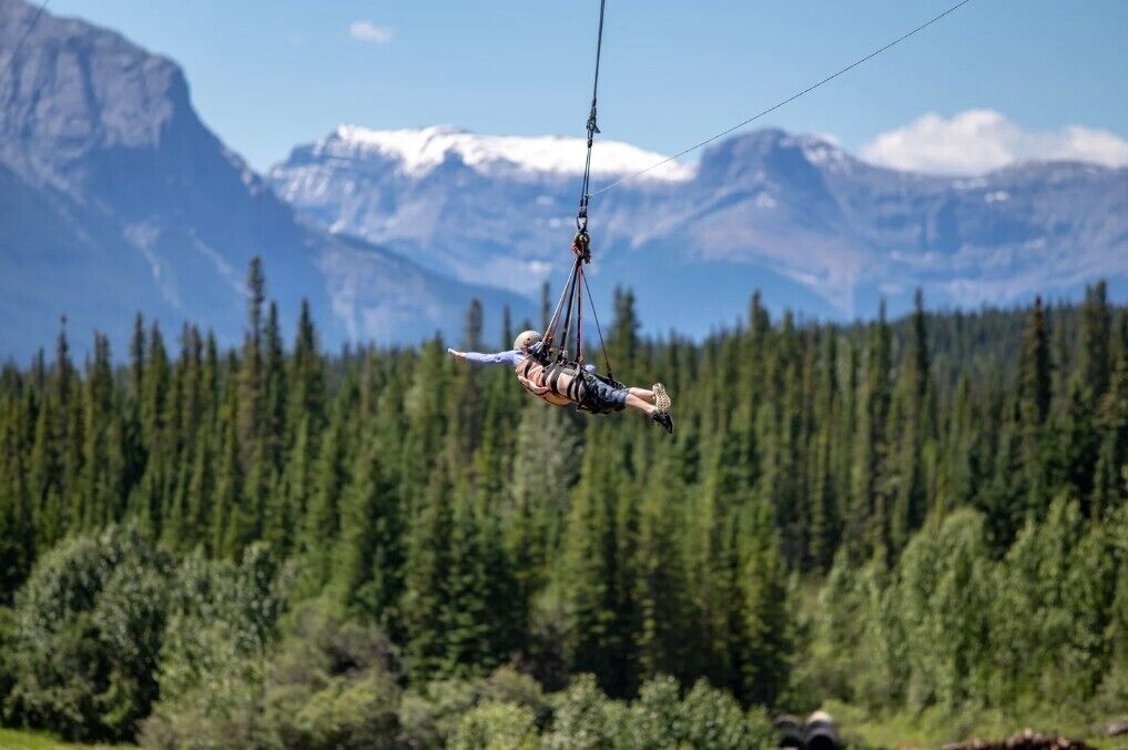 A person suspended in mid-air by a harness, with a mountainous landscape in the background.