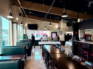 A restaurant with a long wooden table, booths, and hanging pendant lights.