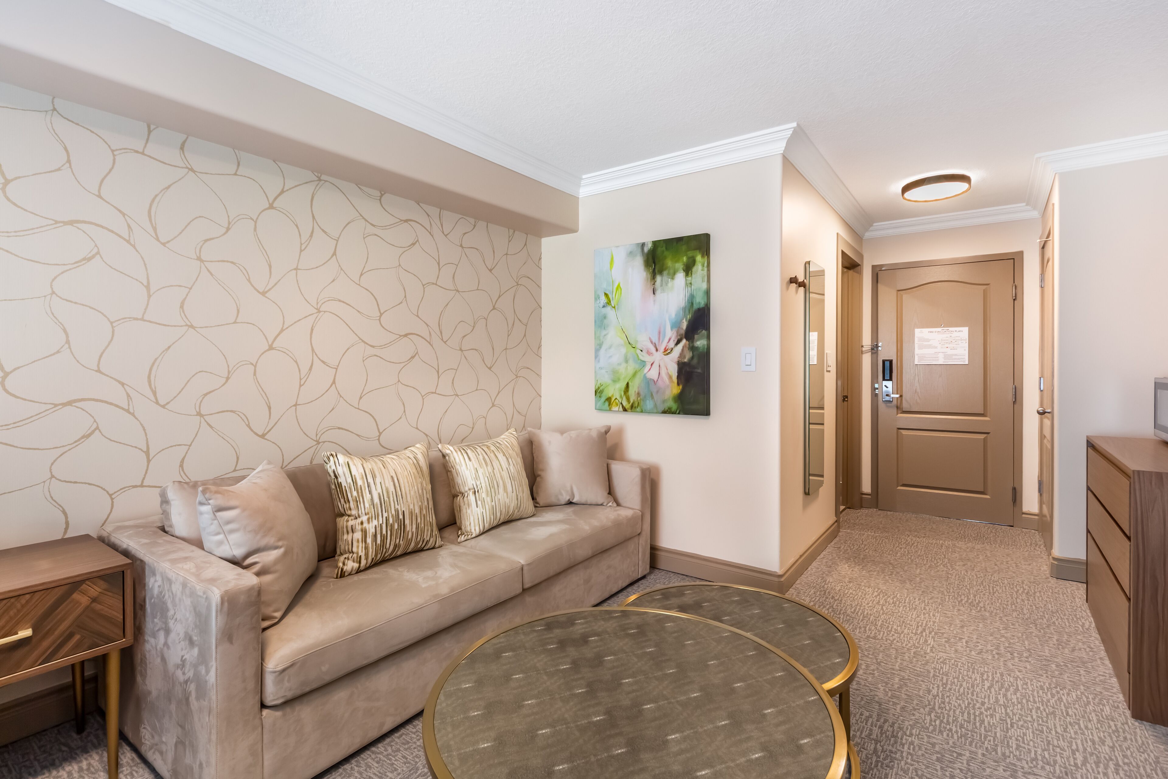 Un salon moderne avec un canapé beige, une table basse ronde et un mur orné d’un motif.