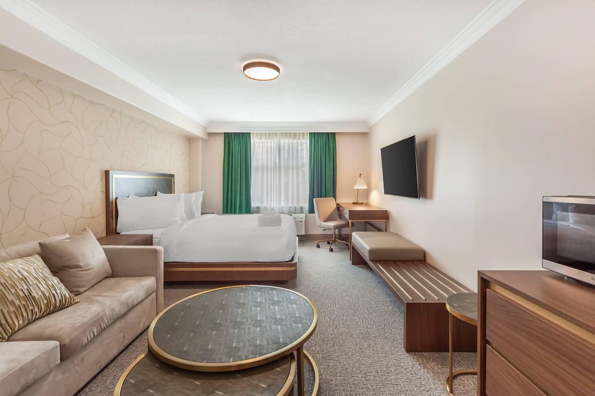 A hotel room with a bed, a sofa, a desk, a TV, and a round table.