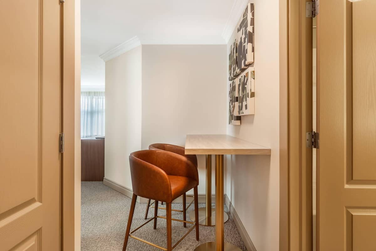 A hallway with a wooden door, a small table with a chair, and a wall-mounted artwork.