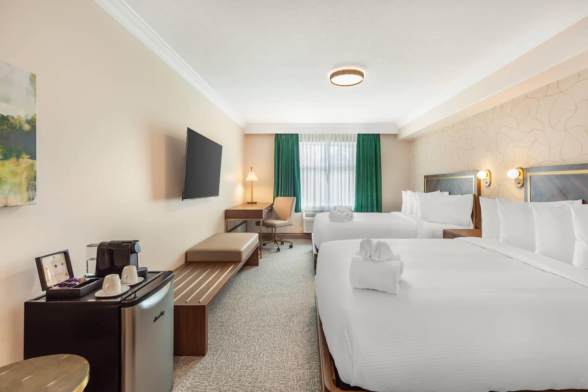A hotel room with a bed, a desk with a coffee machine, a TV, and a window with curtains.