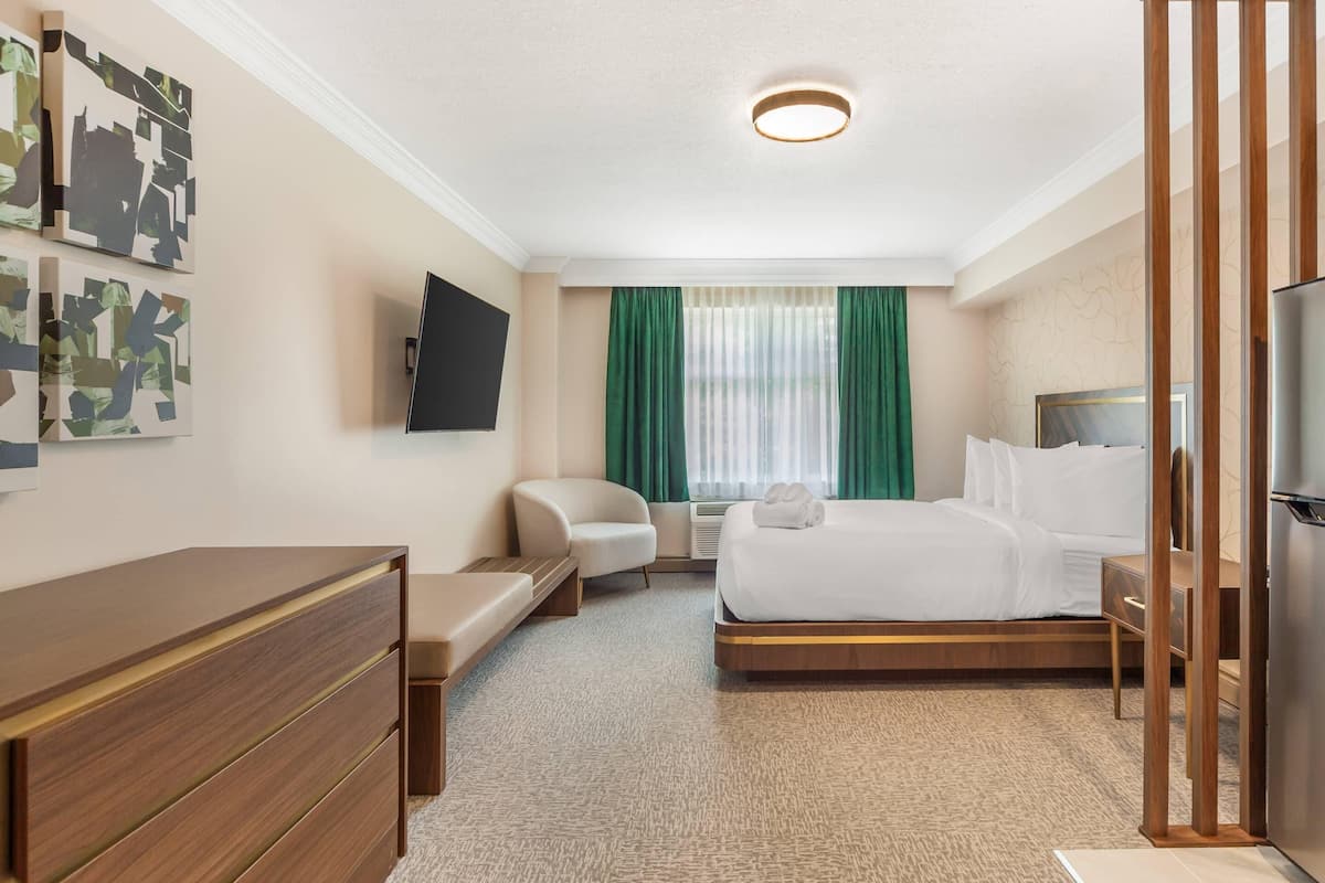 A hotel room with a bed, a desk, a chair, a TV, and a window with curtains.