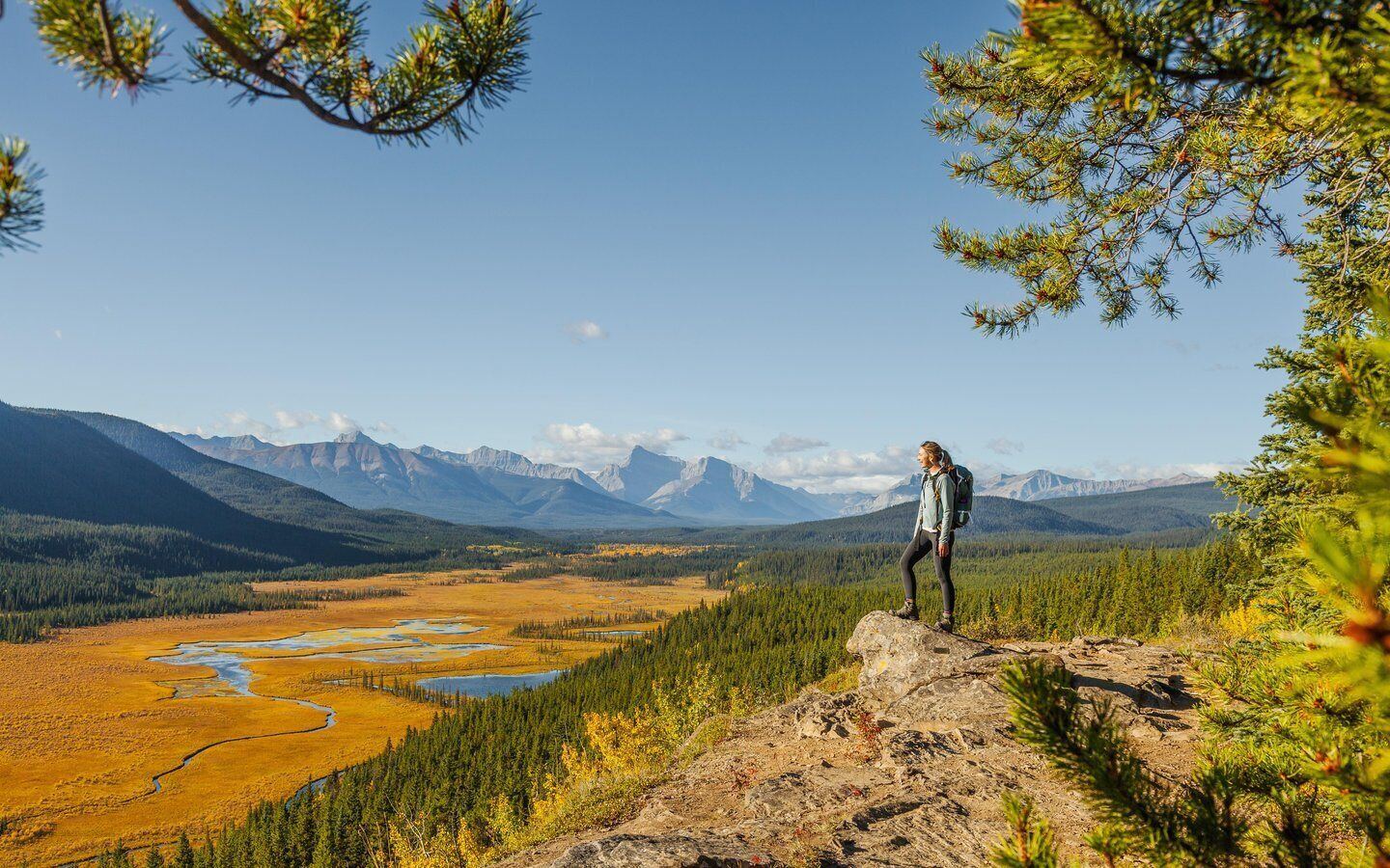 A person standing on a rocky outcrop overlooking a vast landscape with mountains and a river.