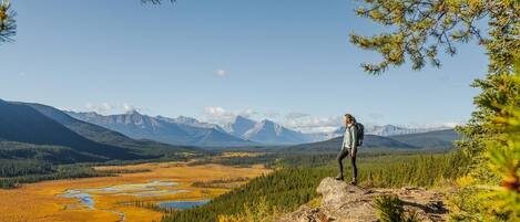 A person standing on a rocky outcrop overlooking a vast landscape with mountains and a river.