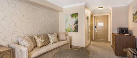 A hotel room with a sofa, two round tables, a cabinet, and a painting on the wall.