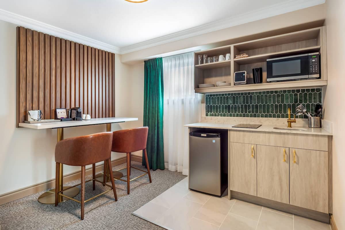 A compact kitchen with a microwave, refrigerator, and bar stools.