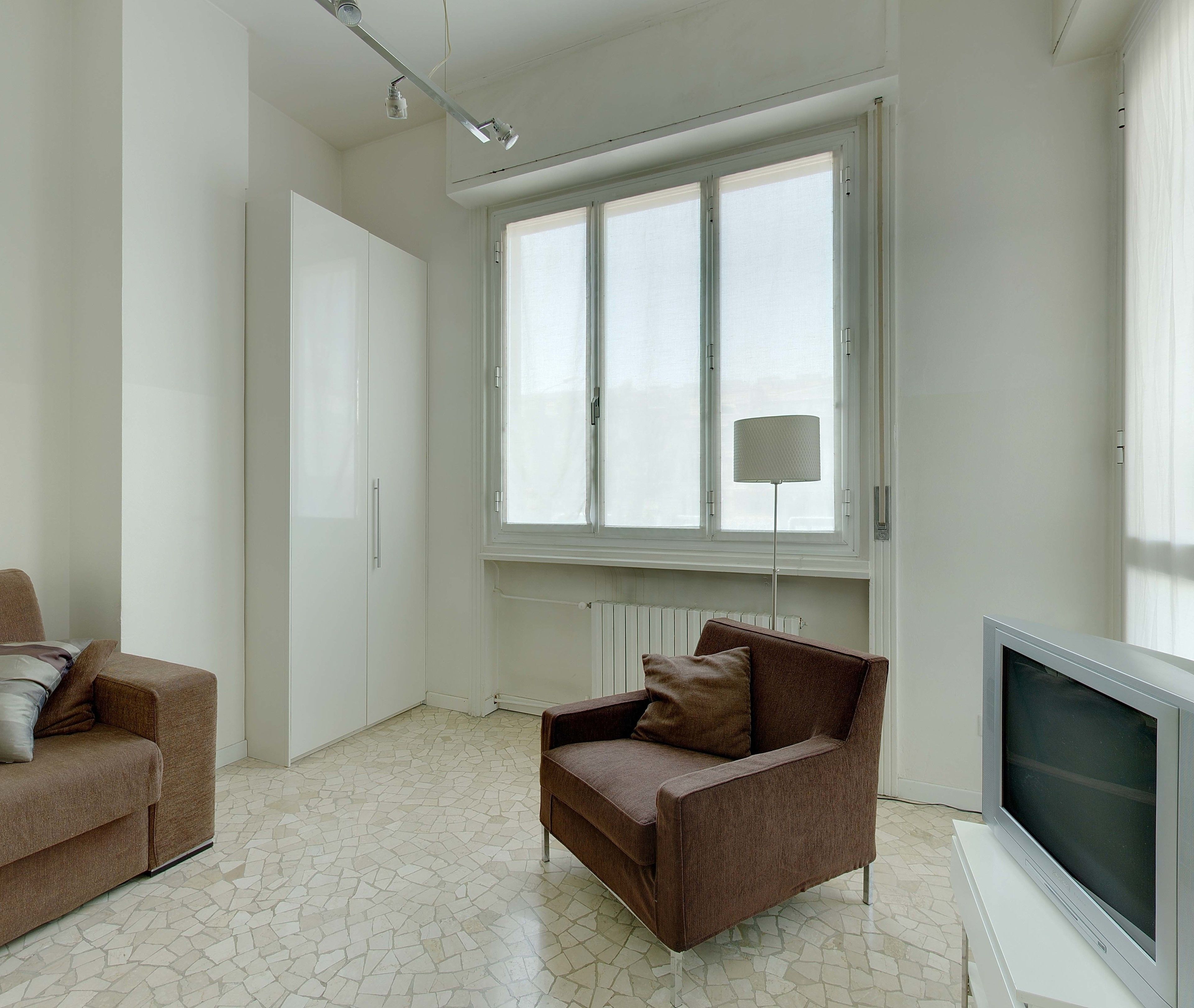 A modern living room with a brown sofa, a television, and a large window with a floor lamp.