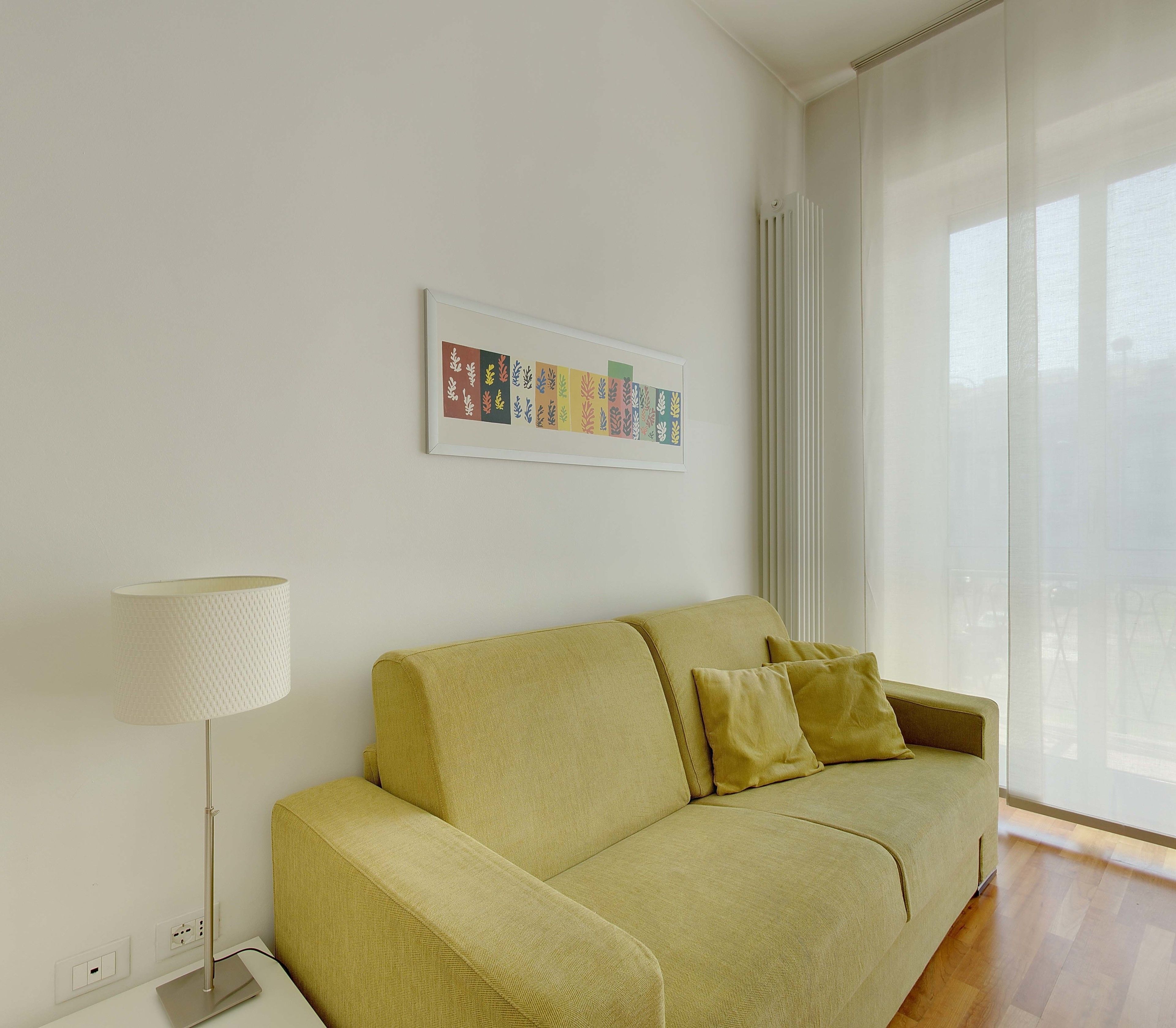 A living room with a sofa, a lamp, and a framed artwork on the wall.