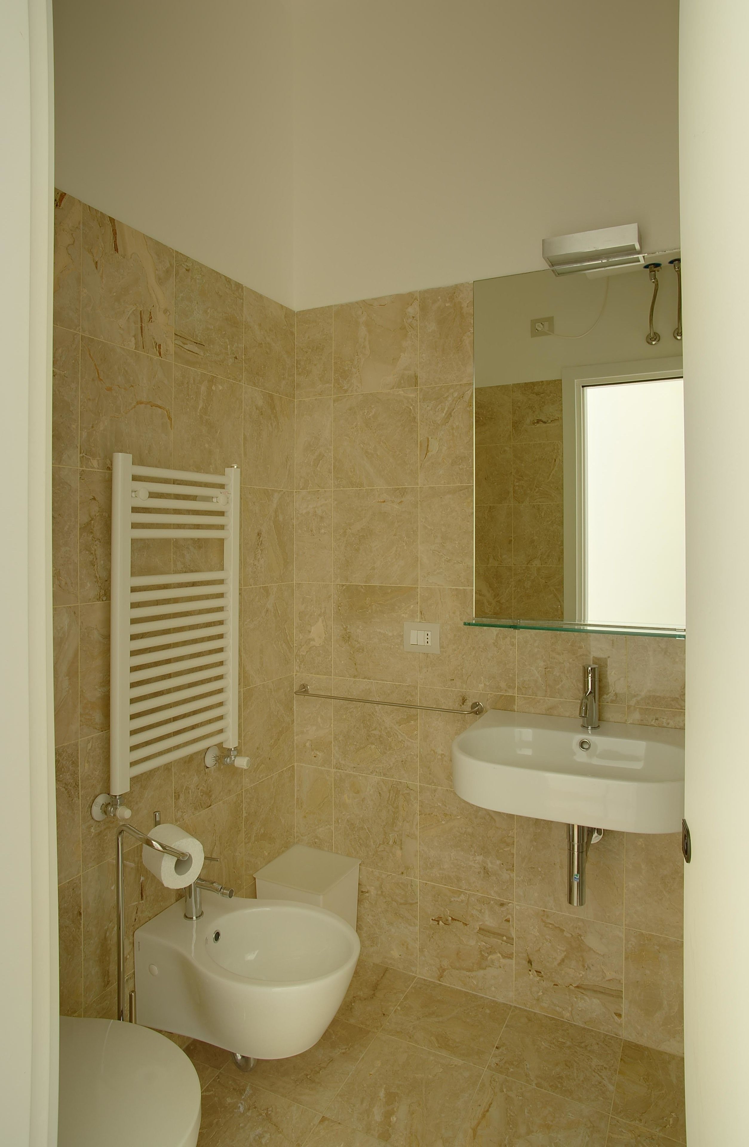 A bathroom with a toilet, bidet, sink, mirror, and towel rack.