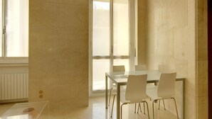 A modern dining area with a glass table, white chairs, and a view through a glass door.