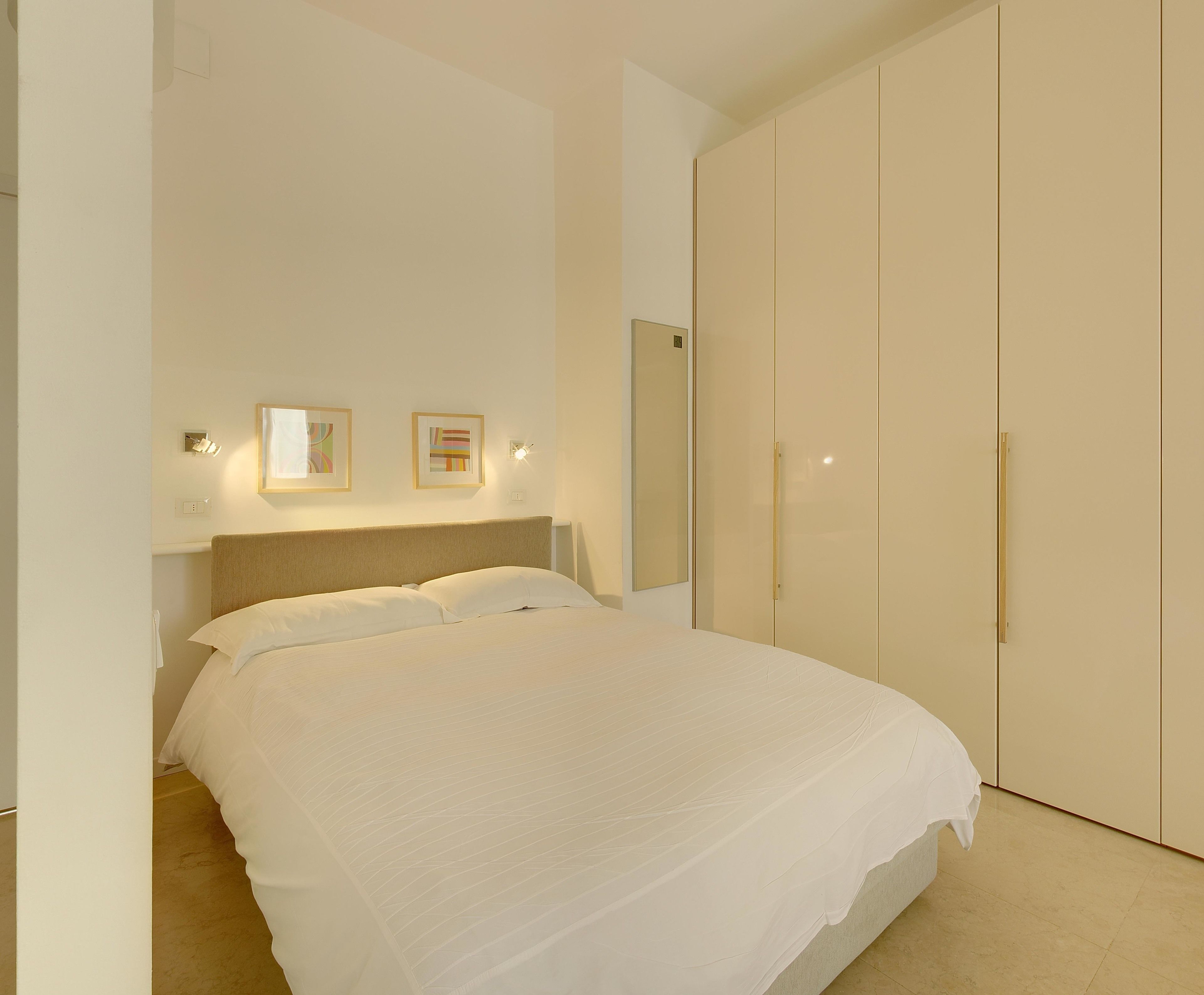 Quarto com cama, guarda-roupa e duas luminárias fixadas na parede.