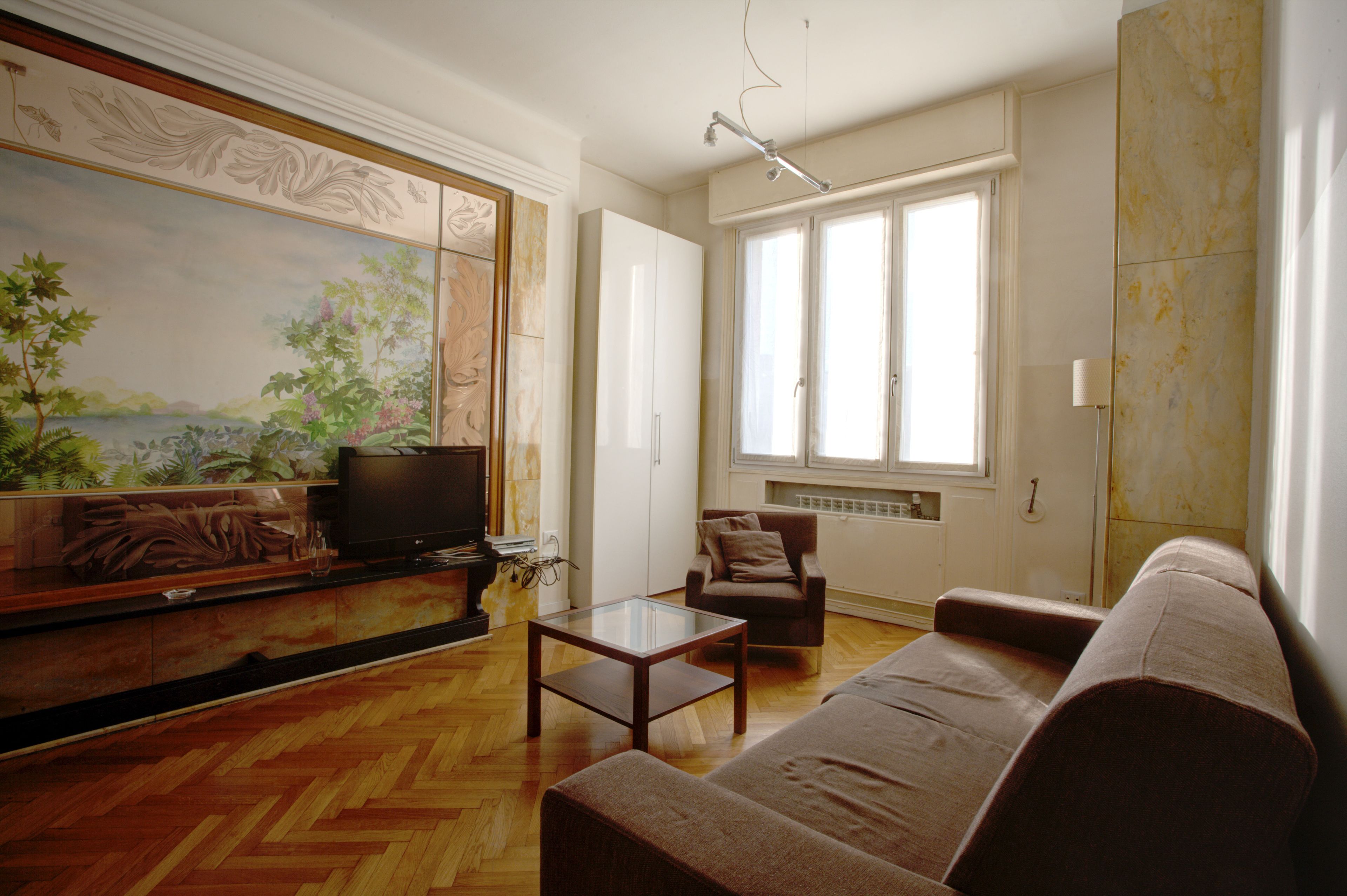 Ein Wohnzimmer mit Holzboden, einer Couch, einem Fernseher und einem Bild an der Wand.