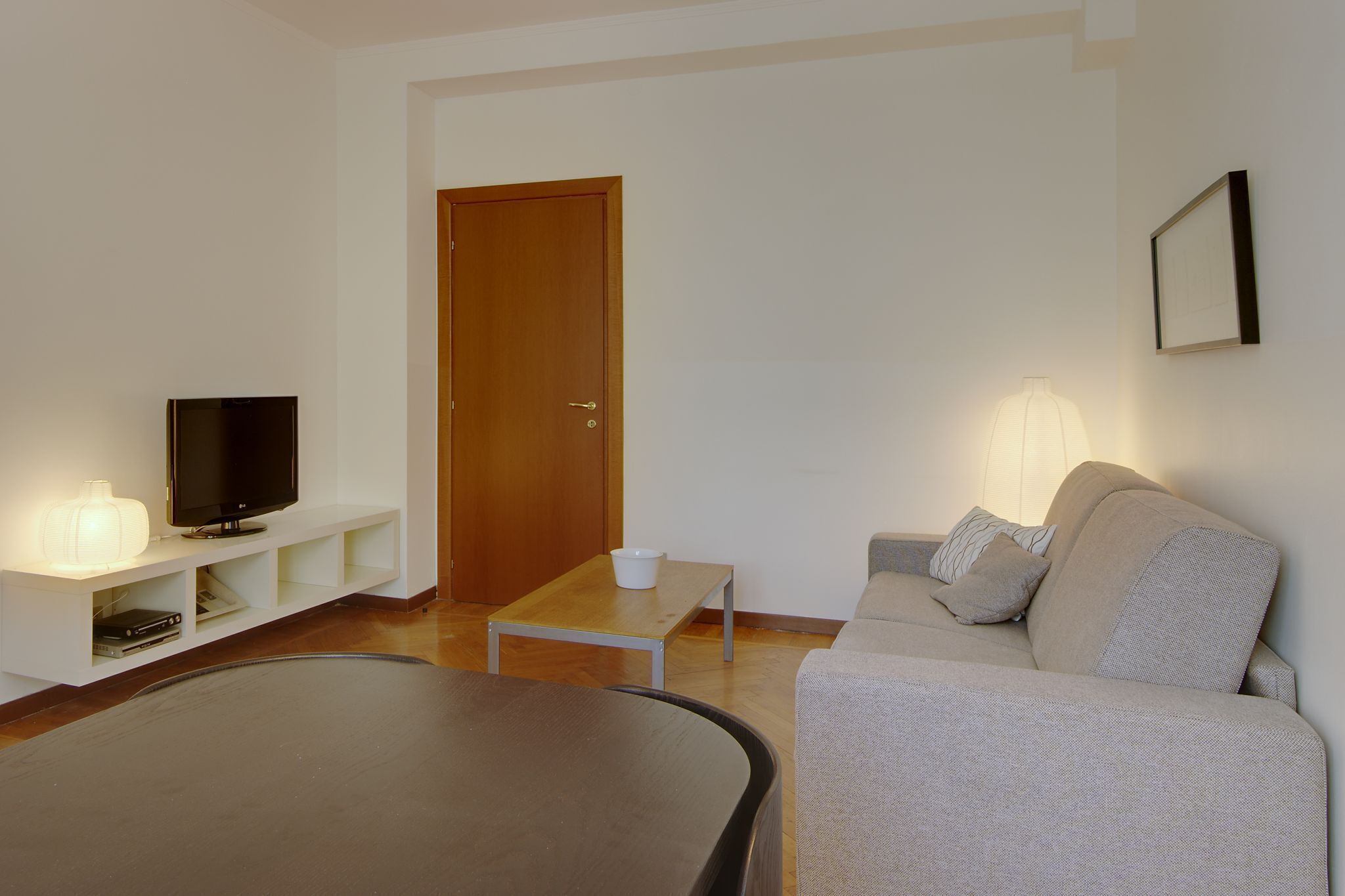A living room with a flat-screen TV, a coffee table, a sofa, and a lamp.