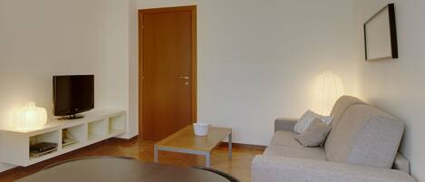A living room with a flat-screen TV, a coffee table, a sofa, and a lamp.