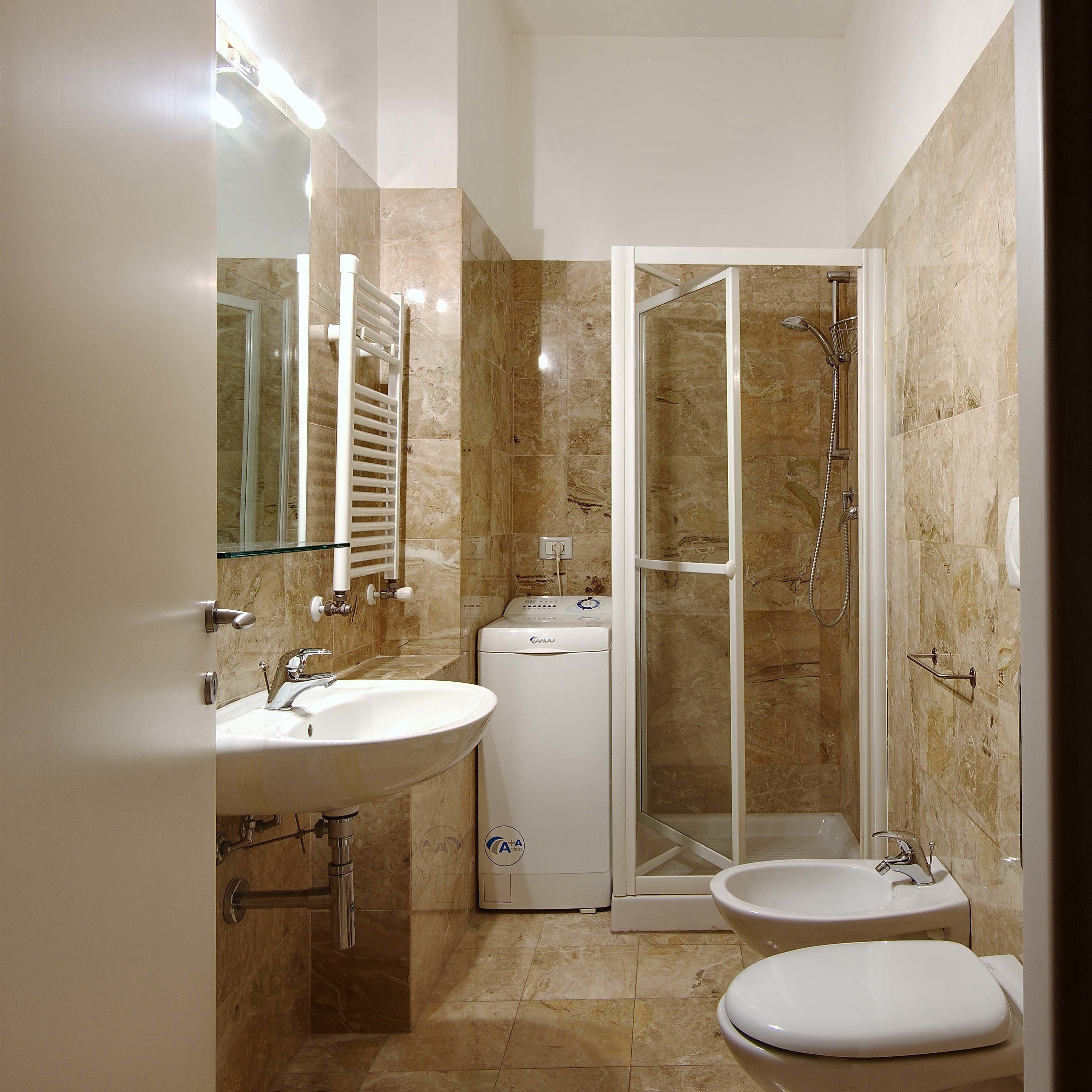 A modern bathroom with two sinks, a glass shower enclosure, and a built-in washing machine.