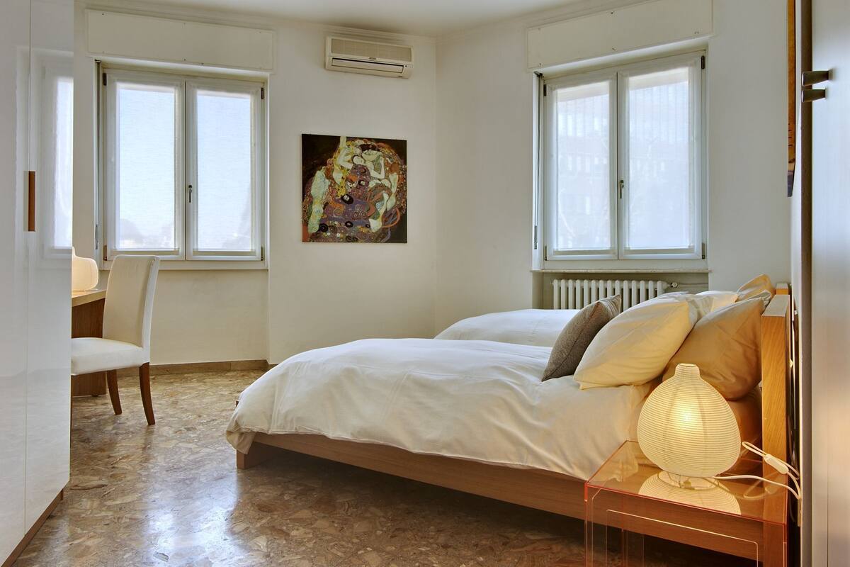 A bedroom with a bed, a chair, a table, and a painting on the wall.