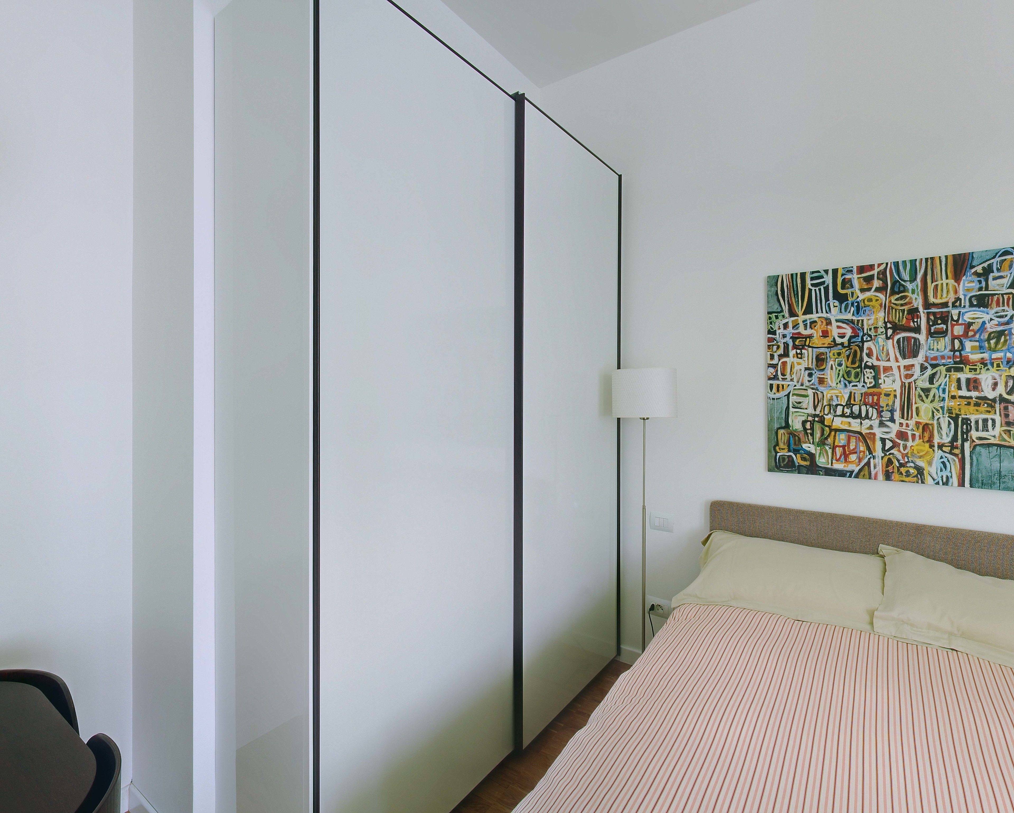 Ein Schlafzimmer mit einem Bett, einem Nachttisch, einer Lampe, einem Bild an der Wand und einer Schiebetür.