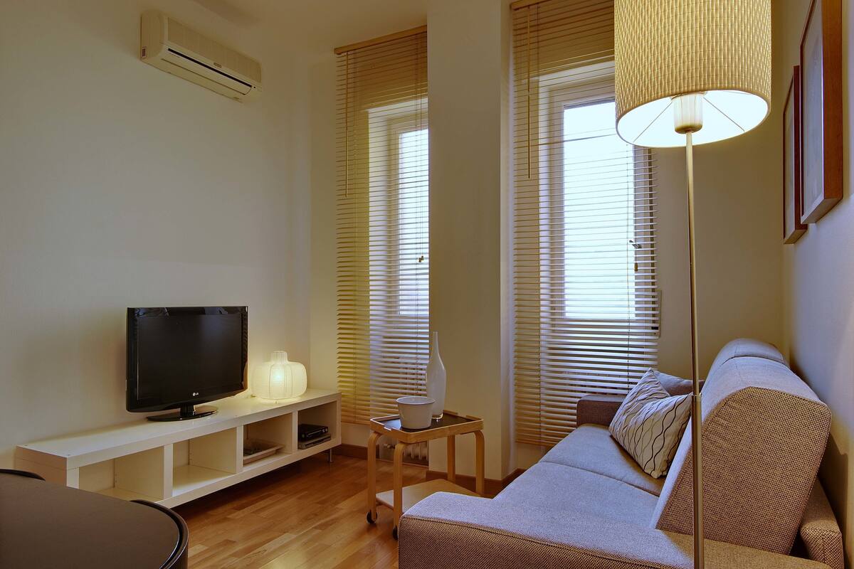 A living room with a TV, a sofa, a lamp, and a small table.